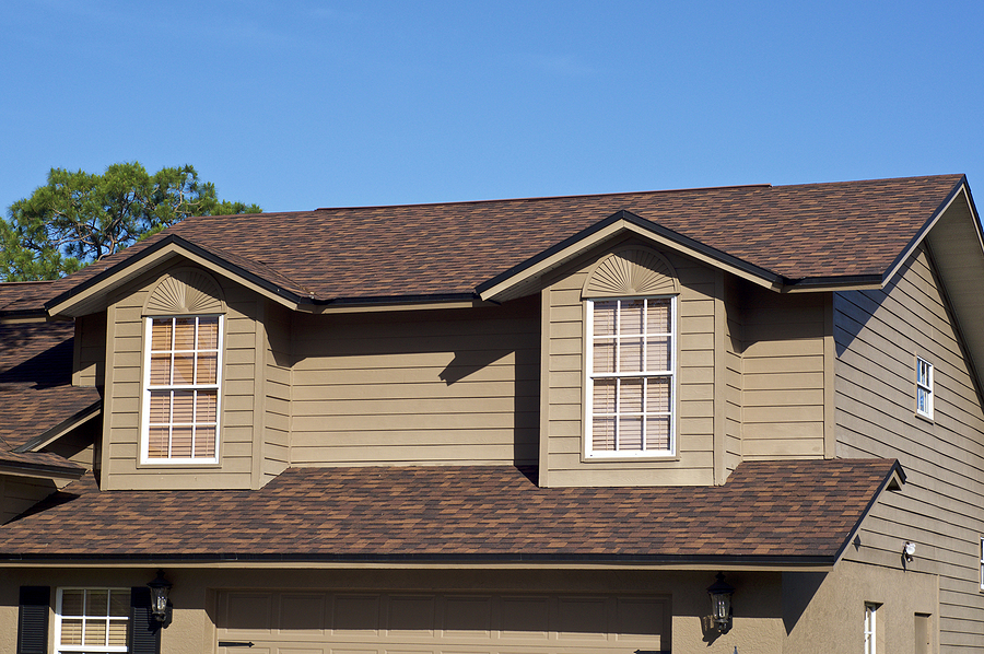 View of brown two story house against blue sky with gables windows and clean roof. View of brown two story house against blue sky with gables windows and clean roof.